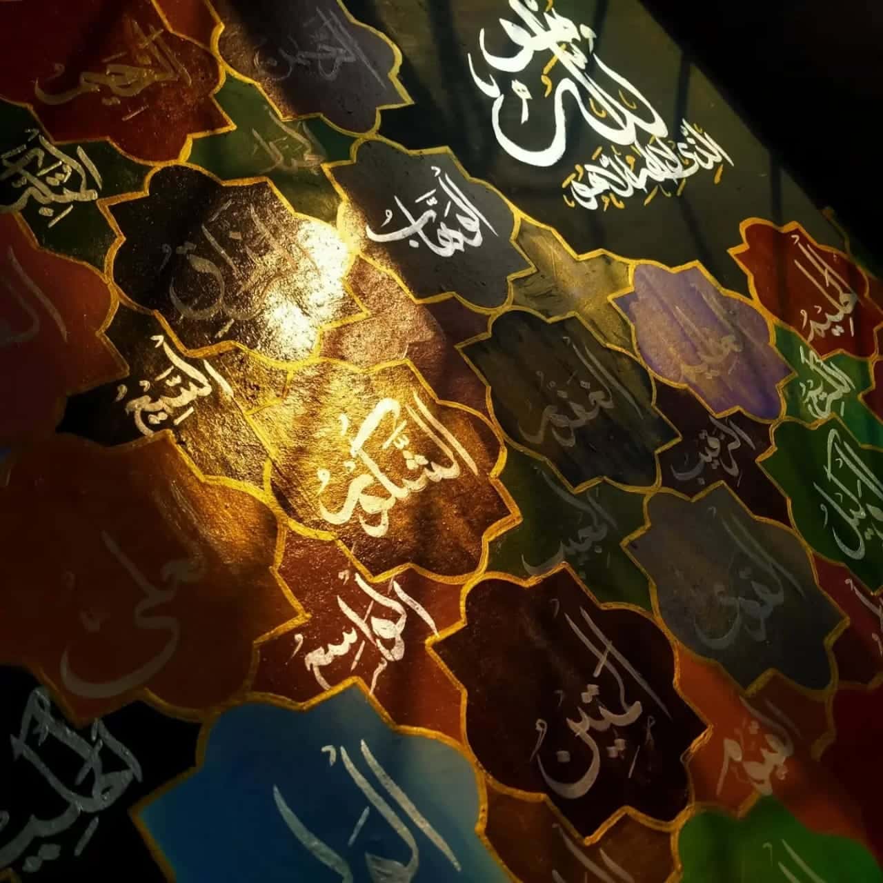 Close view of 99 Names of Allah calligraphy in jewel-tone geometric medallions with white and gold Arabic lettering